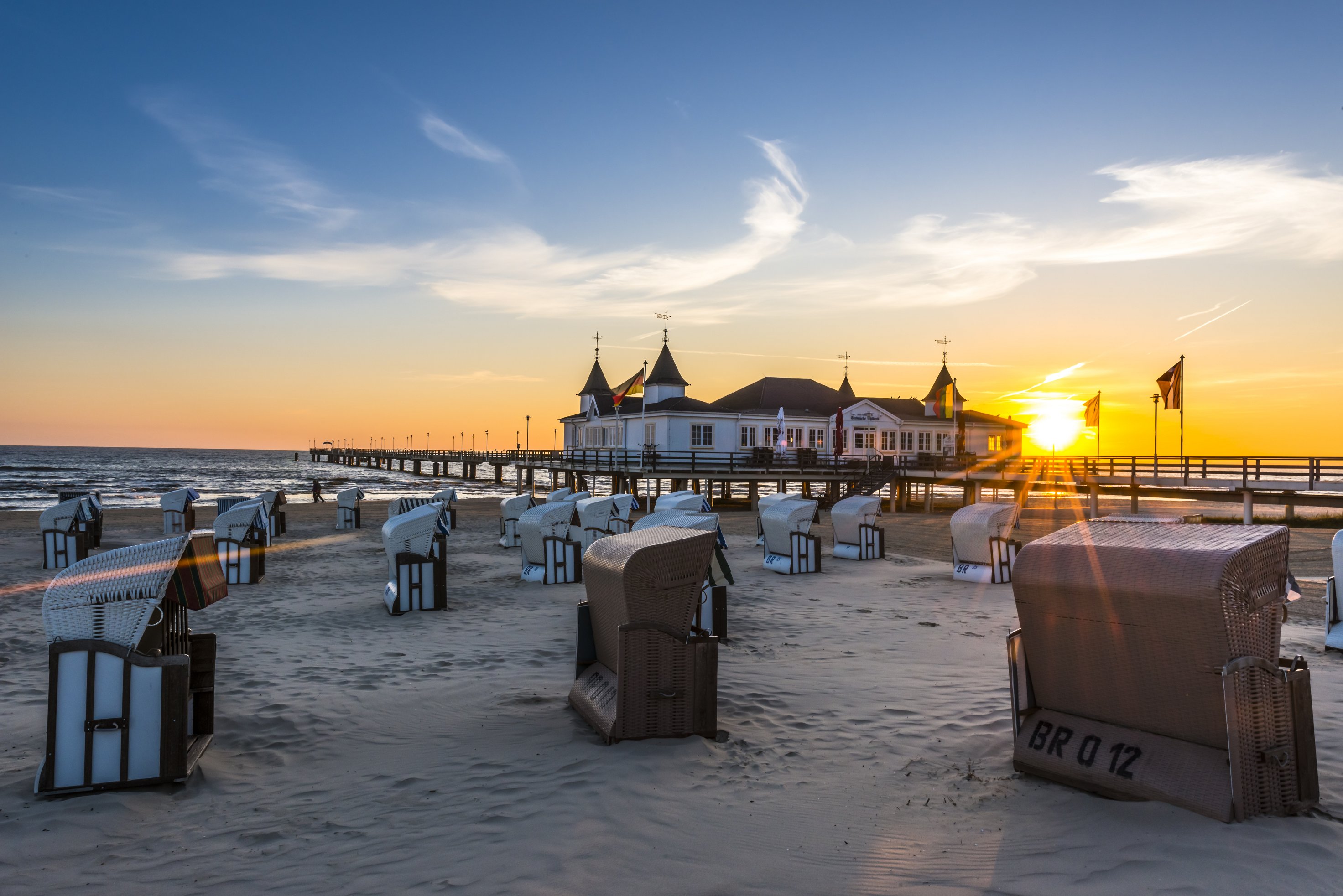 Blick auf den Strand im Seebad Ahlbeck bei Sonnenaufgang. Im Hintergrund ist die Seebrücke, im Vordergrund stehen viele Strandkörbe